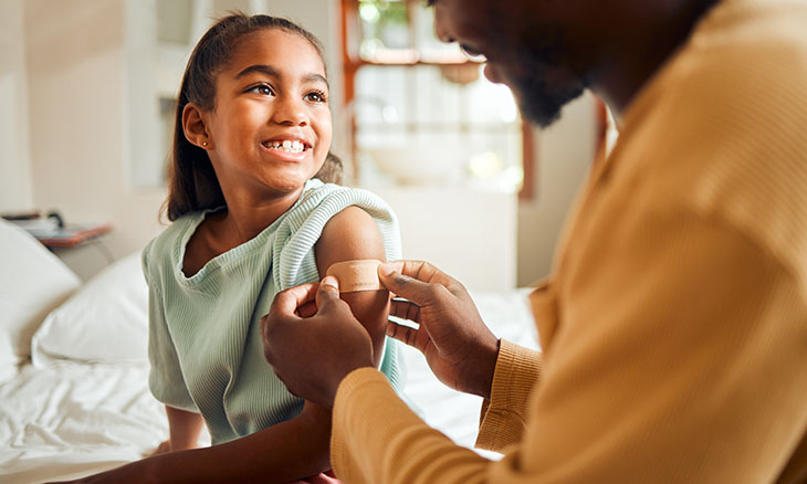 A dad puts a bandage on his daughter's arm